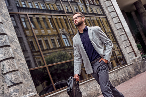 Hurry for meeting. Young businessman walking on the city street holding briefcase hand in pocket confident © Friends Stock