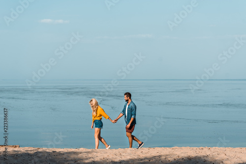 girlfriend and boyfriend holding hands and walking on sandy beach