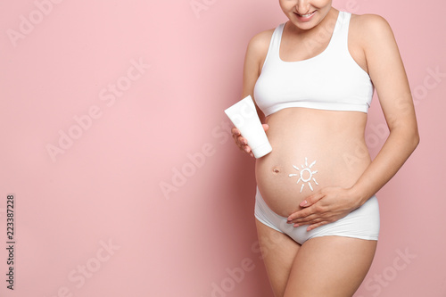 Sun painted with body cream on pregnant woman's belly against color background, closeup. Space for text