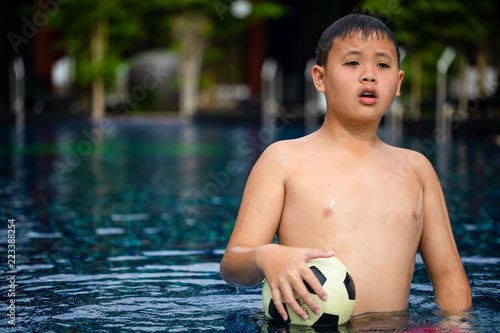 Soaking wet Asian boy carry ball in swimming pool