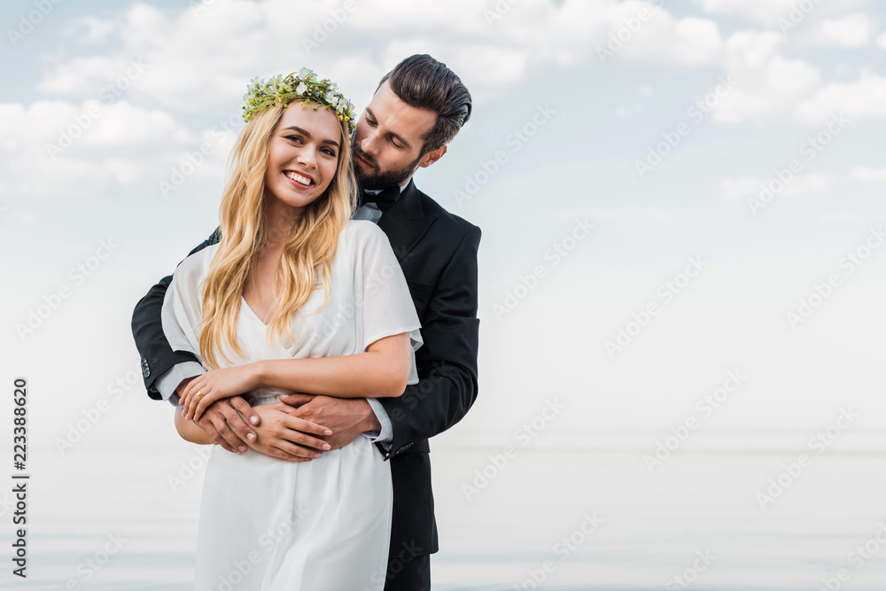 handsome groom in suit hugging attractive bride on beach handsome groom in suit hugging attractive bride on beach