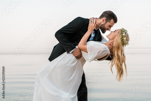 affectionate wedding couple going to kiss on beach photo