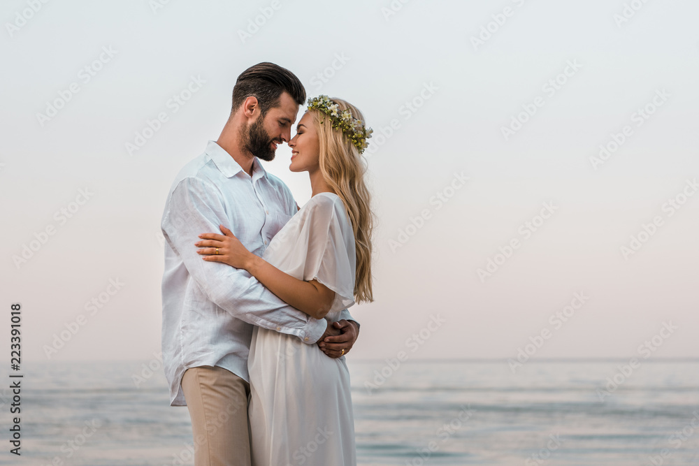 side view of bride and groom hugging and touching with noses on beach