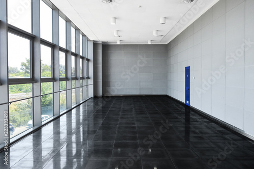 Big empty office space with window wall. Day light illumination. Grey tones interior design. Dark and light color scheme. Window reflection on glossy floor. Perspective front view. Modern business