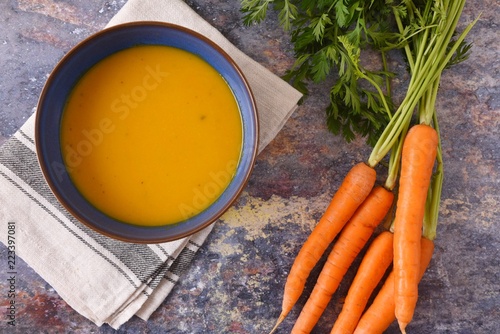 Bowl of vegetable soup surrounded by a bunch of carrots