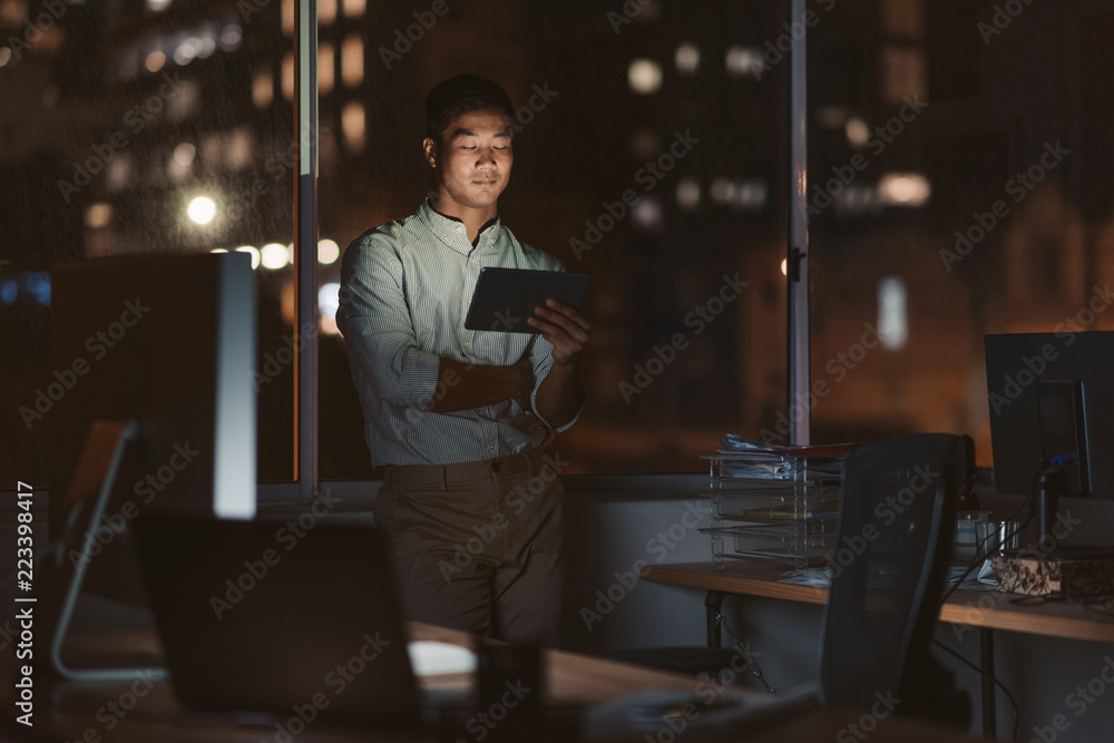 Fototapeta premium Asian businessman working late in his office with a tablet