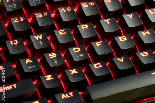 wired mechanical gaming keyboard with LED illuminated keys; LED light glowing in the background 