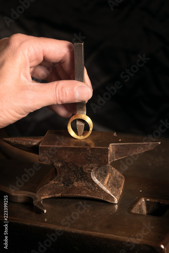 Canvas Print goldsmith hand punches a hallmark into a golden ring on a small anvil, copy spac