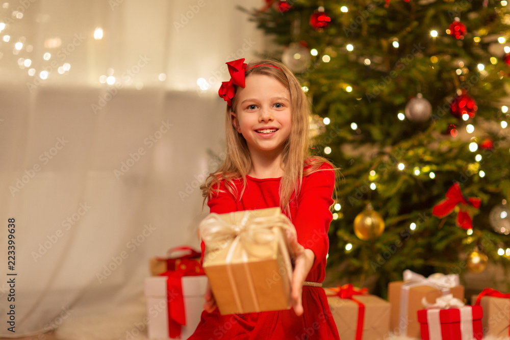 christmas, holidays and childhood concept - smiling girl in red dress with gift box at home