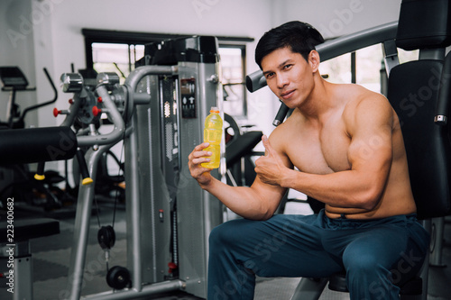 Asian fit man with energy drink relaxing and drinking in the gym. Sport and fittness concept.And Asian handsome muscles are tired, so drink Electrolyte drink.