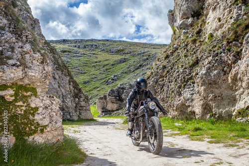 Biker with black leather clothes, ride  his custom rat motorcycle in a desolated mountain land. Post apocalyptic concept photo