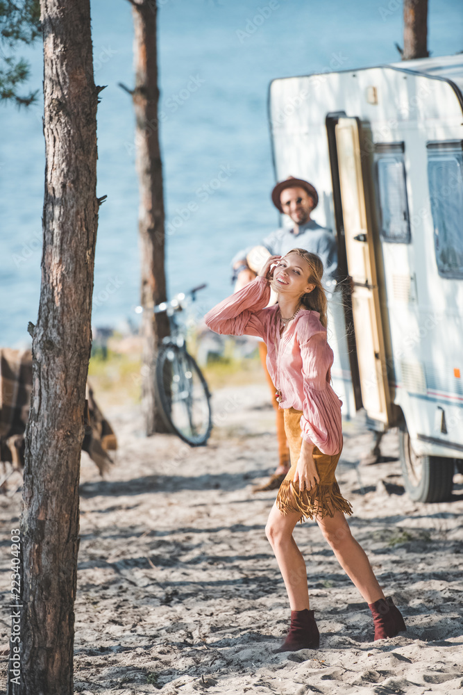 attractive happy girl dancing while man playing guitar near campervan