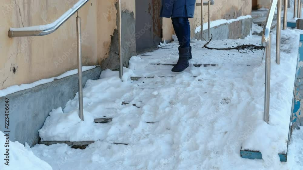 Slippery stairs. Unrecognizable woman in a blue down jacket walking down a snowy staircase. Slippery stairs. Unrecognizable woman in a blue down jacket walking down a snowy staircase.