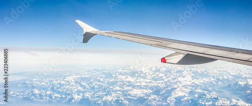 Panoramic image of a plane wing over snowy alpine mountains on a sunny day