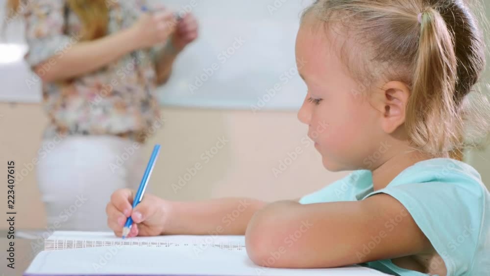 Little cute girl sits in classroom and studies with teacher in exercise book Little cute girl sits in classroom and studies with teacher in exercise book