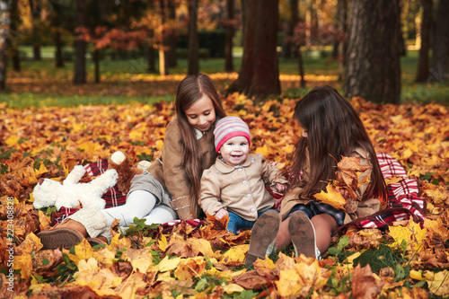 Three happy little sisters having fun playing with fallen golden leaves