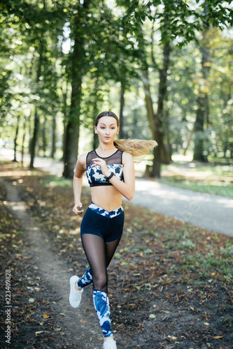 Fototapeta Naklejka Na Ścianę i Meble -  Young lady running. Woman runner running through the spring park road. Workout in a Park. Beautiful fit Girl. Fitness model outdoors. Weight Loss