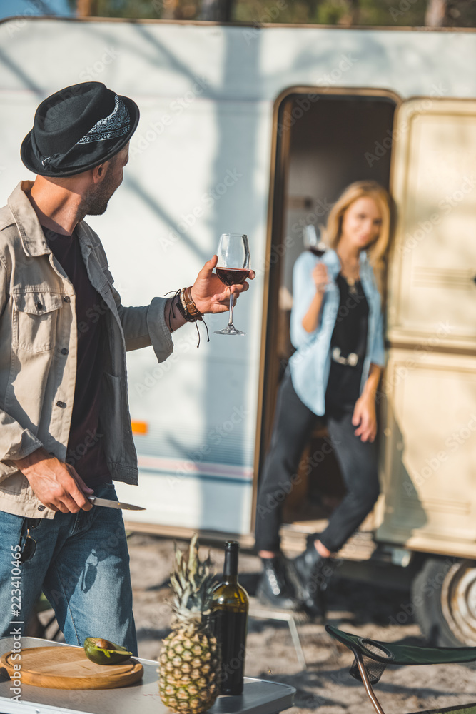 Fototapeta premium selective focus of man with glass of wine looking at girlfriend near campervan