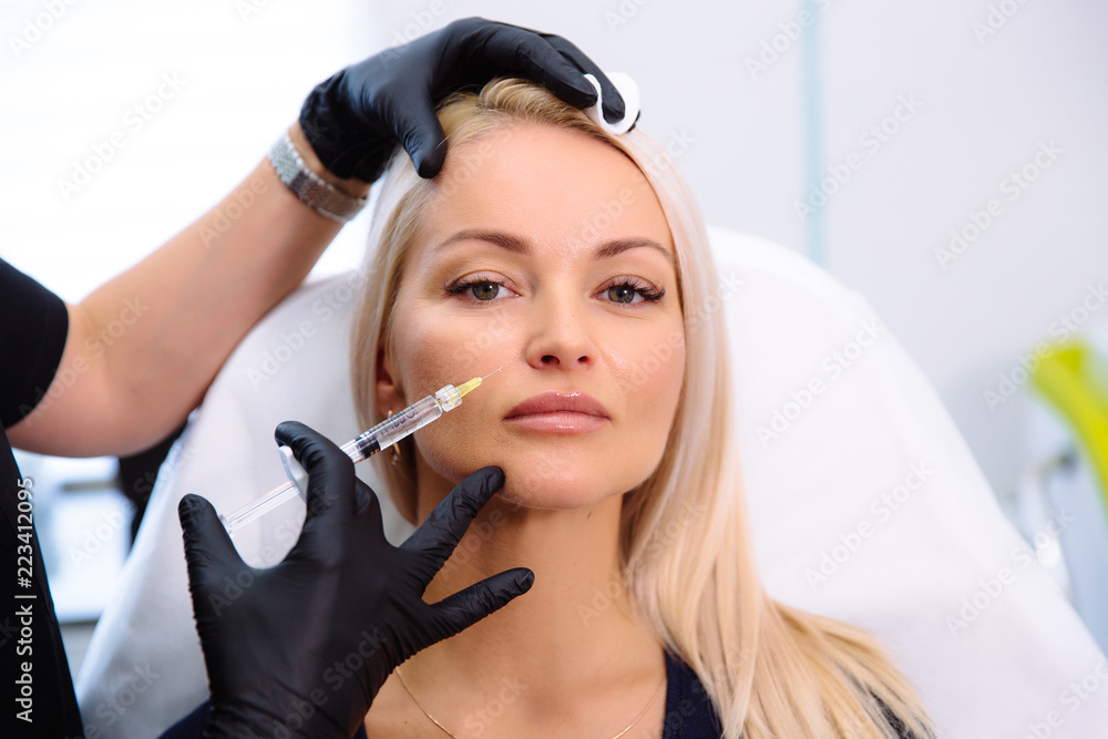 Close-up beautiful female face and cosmetologist's hands with syringe during facial beauty injections. Rejuvenation and hydratation. Cosmetology concept in clinic.