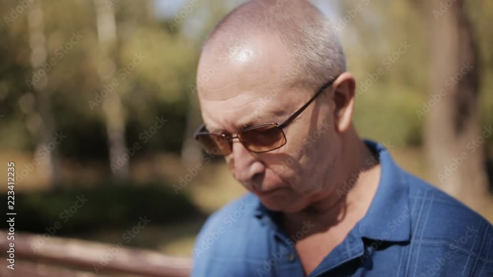 An elderly man with glasses reading an e-book on a Park bench An elderly man with glasses reading an e-book on a Park bench