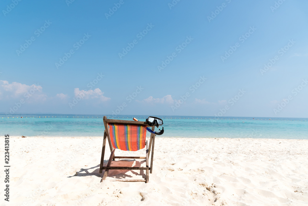 Diving mask hanging in a bright colored wooden beach chair on island tropical beach