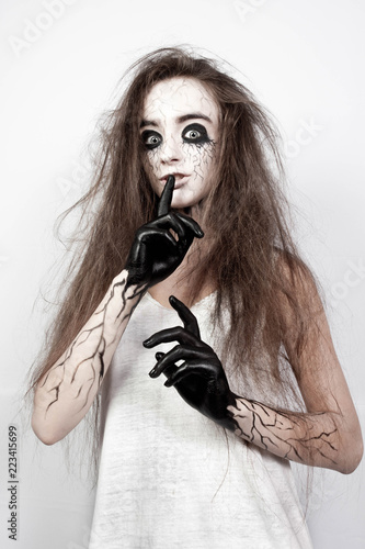crazy girl with disheveled hair, black eyes and veins shows her finger shh. Halloween concept.