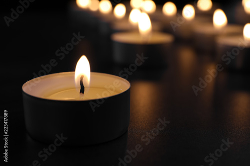 Burning candle on table in darkness  closeup with space for text. Funeral symbol