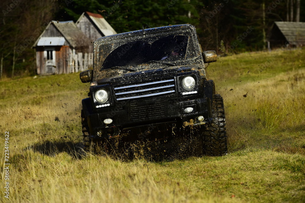 Off road car in black color takes part in racing. Cross country rallying or rally raid near countryside hut aside forest. SUV crossing grass terrain. Extreme and four wheel drive concept