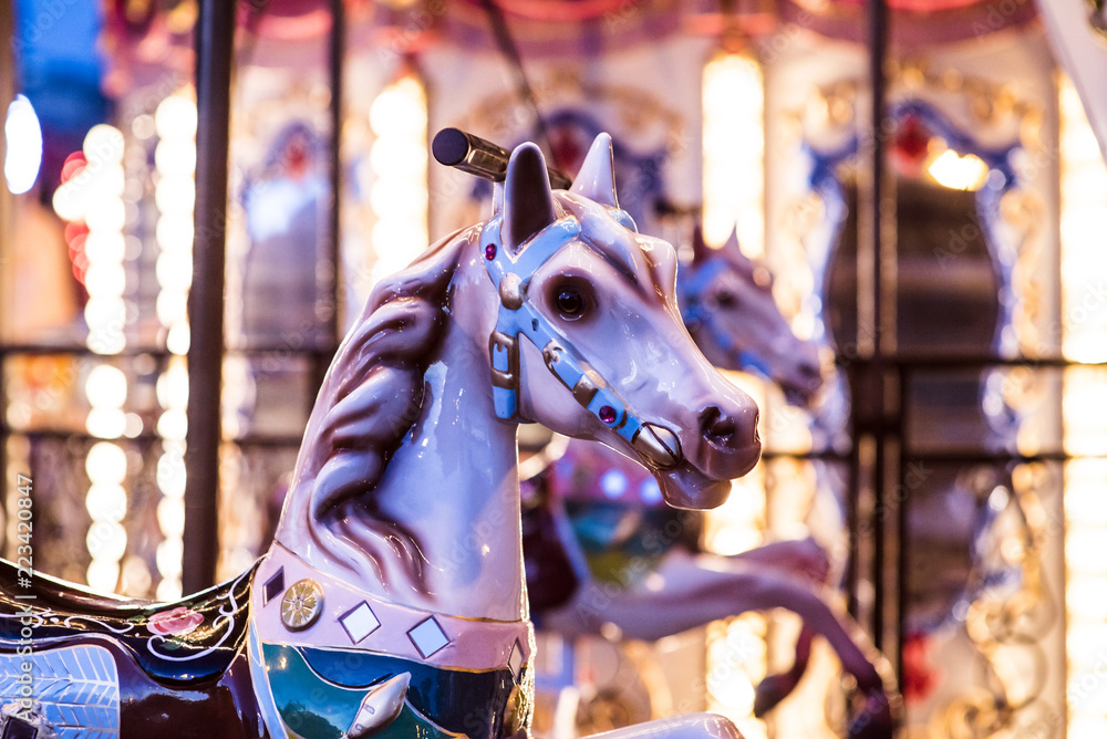 Brilliant vintage merry-go-round wooden horses against the background of Children's Carousel at night time.