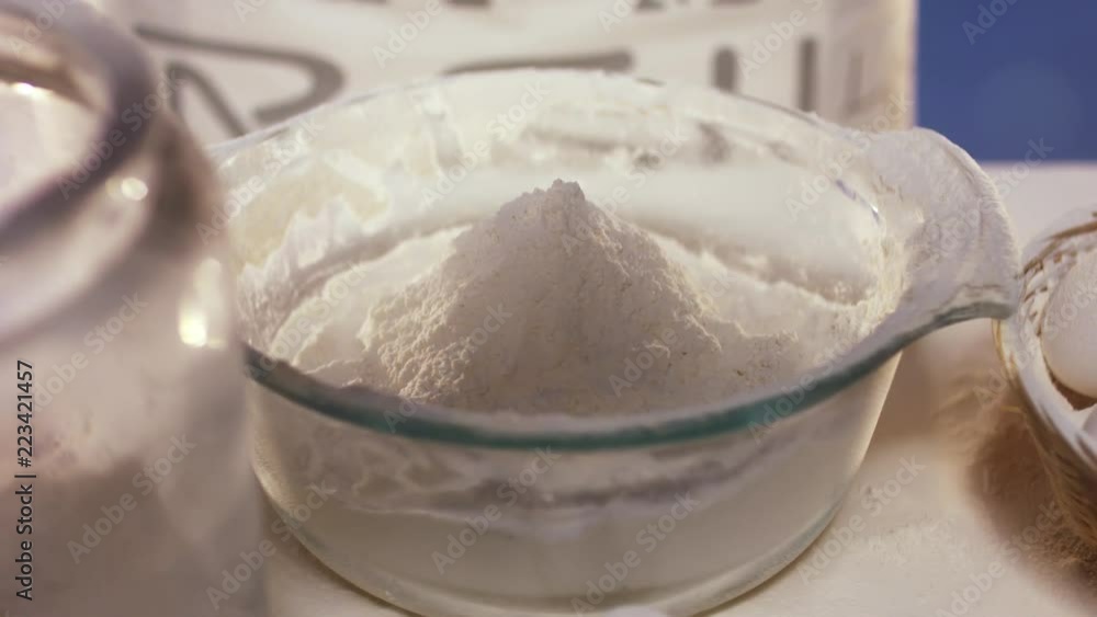 Slow motion of dropping then falling egg white and yolk into flour in glassy round plate with wide edges, standing on white cooking table with colorful blurry background Slow motion of dropping then falling egg white and yolk into flour in glassy round plate with wide edges, standing on white cooking table with colorful blurry background