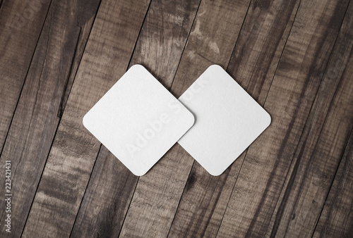 Two blank square beer coasters on wood background. Flat lay.