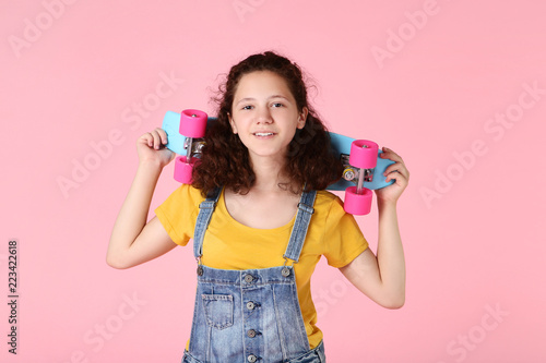 Young girl with skateboard on pink background
