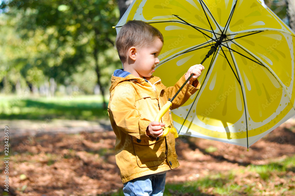 Cute toddler boy in yellow rubber boots yellow raincoat holding a