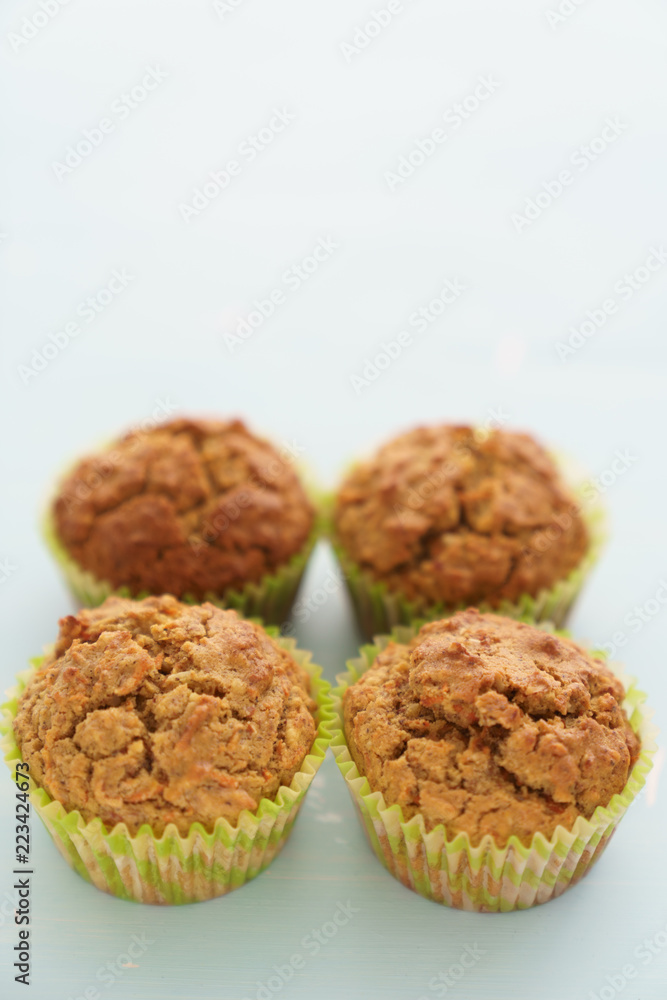 Four carrot muffins on a light blue background. Space on top, high resolution