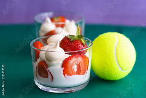 Wimbledon inspired whipped cream, meringues and fresh strawberries in a glass bowl on a green and violet background with a tennis ball photo