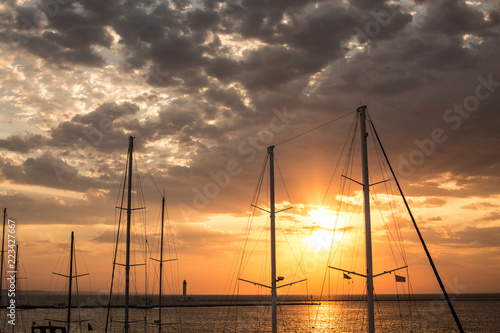 Masts of yachts in the port at sunrise against the background of the sea and the cloudy sky photo