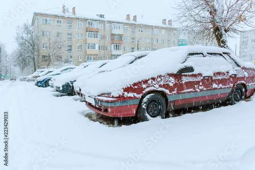 Snowfall and snow-covered cars stand in the courtyard of a multi-storey building. Drifts. 