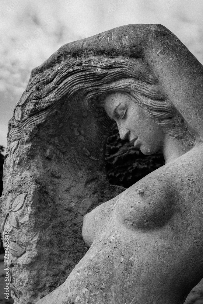 Fototapeta Female stone sculpture with a naked breast with a raised up hand touches the hair against the sky
