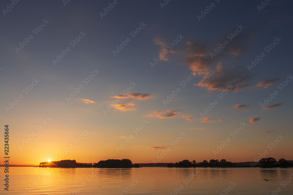 Landscape of sunset over the horizon on a beautiful lake. Colorful sky with clouds over the surface of the lake in the evening. Vivid sun sets over the horizon. Summer Landscape.