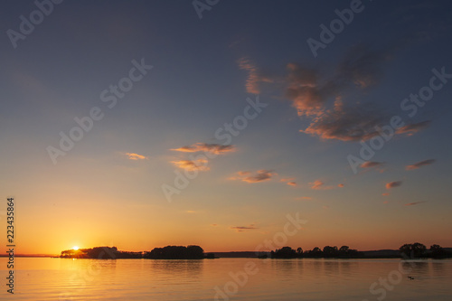 Landscape of sunset over the horizon on a beautiful lake. Colorful sky with clouds over the surface of the lake in the evening. Vivid sun sets over the horizon. Summer Landscape. © dzmitrock87