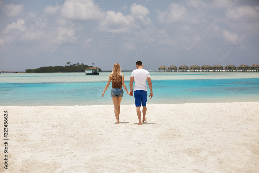 Back view of couple holding hands and walking to the blue ocean lagoon on Maldives at luxury spa resort. Travel and honeymoon concept.