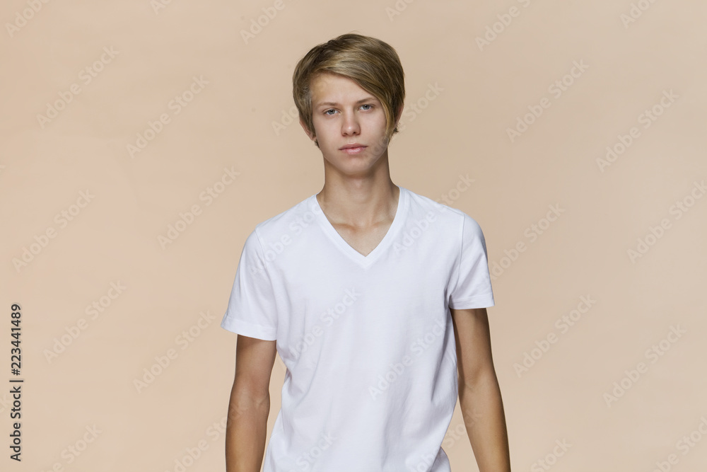 Serious male with attractive look, wearing T-shirt, posing against light brown blank wall. Happy man with hair bun showing positive emotions Serious male with attractive look, wearing T-shirt, posing against light brown blank wall. Happy man with hair bun showing positive emotions
