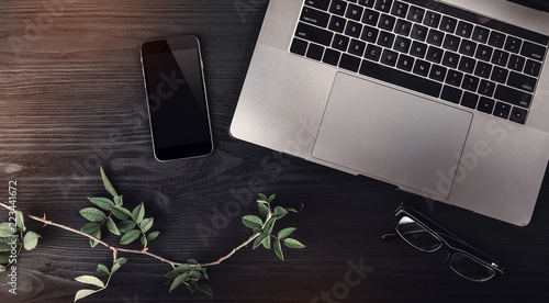 Wallpaper Mural Modern workspace with laptop, mobile phone, eyeglasses and rose branch on wooden background. Top view, light effect Torontodigital.ca
