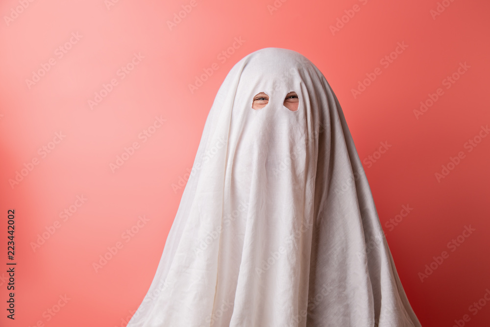 young child dressed in a ghost costume for halloween on pink background