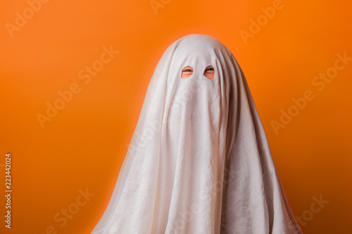Fotótapéta young child dressed in a ghost costume for halloween on orange background