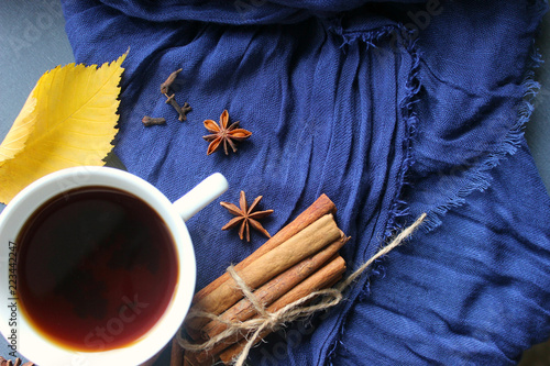 Autumn still-life. A Cup of hot tea yellow autumn leaf and spices, cinnamon sticks, anise, cloves on a blue scarf background. Warm warming drink, comfort, relaxation, relaxing drink.Tea, coffee with s photo