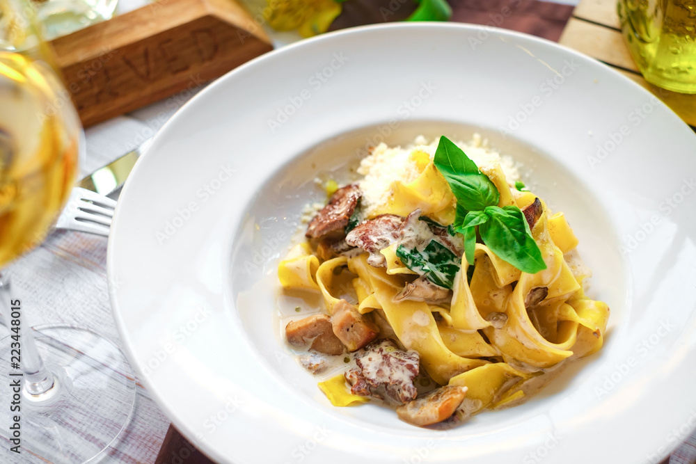 pasta tagliatelle with mushrooms in cream sauce on a white plate, served in a restaurant with wine