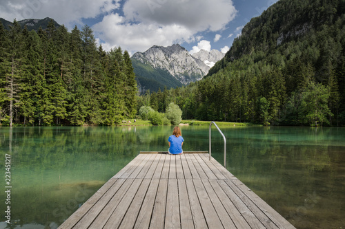 Young woman sitting on wooden footbridge in scenic mountain lake plansarsko, slovenia photo