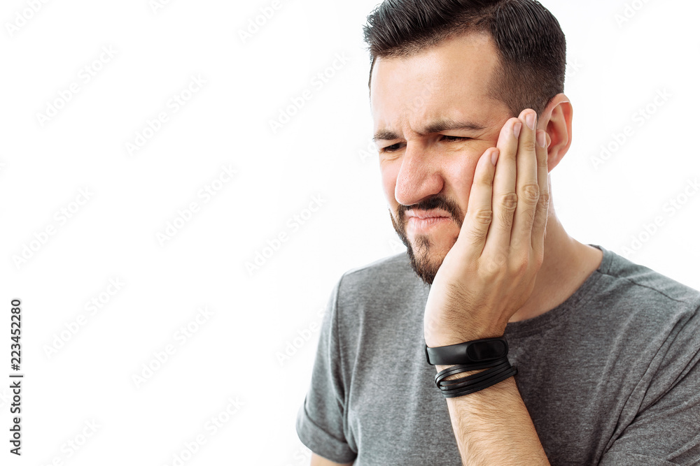 Sad bearded young man standing and having toothache on white background Sad bearded young man standing and having toothache on white background