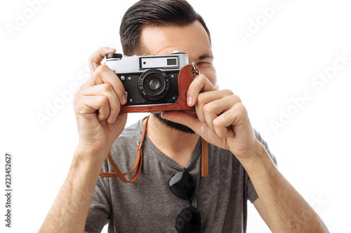 Portrait of a handsome photographer guy with a beard, taking pictures with a camera standing on a white background